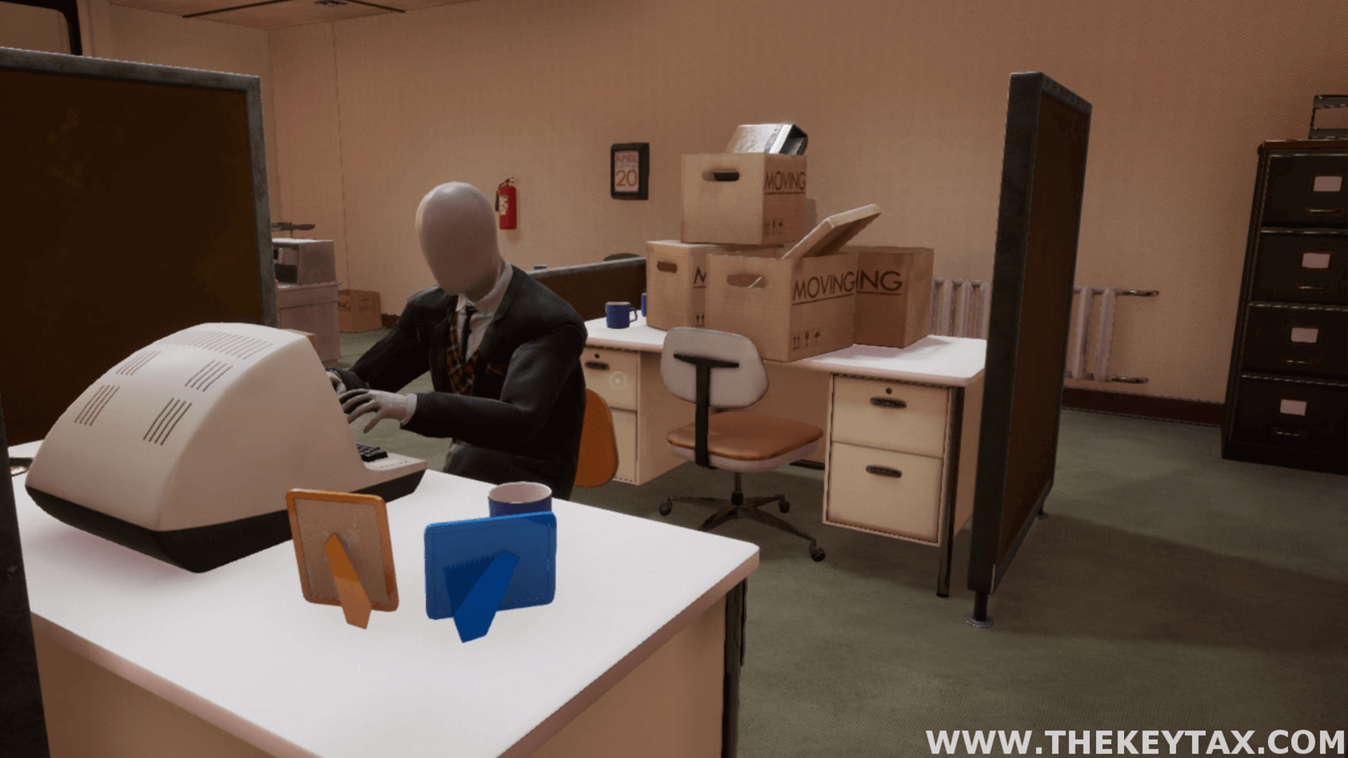 A mannequin is seen sitting at a desk working on a computer, with two picture frames and a cup on their desk.